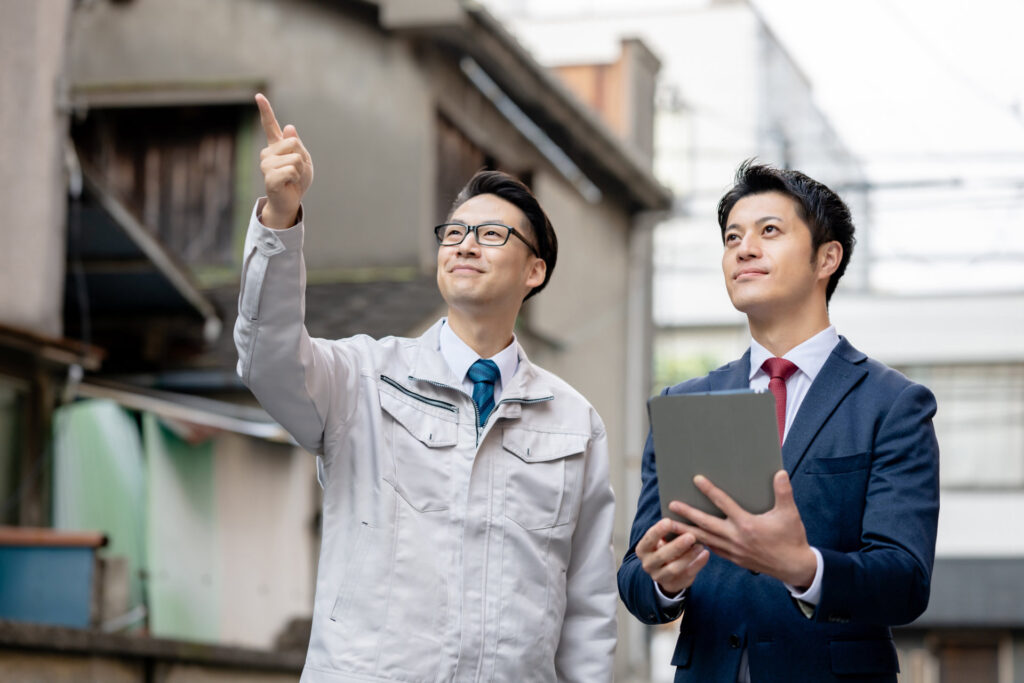 住宅街で上を指さす作業着の男性とタブレットを持つ男性
