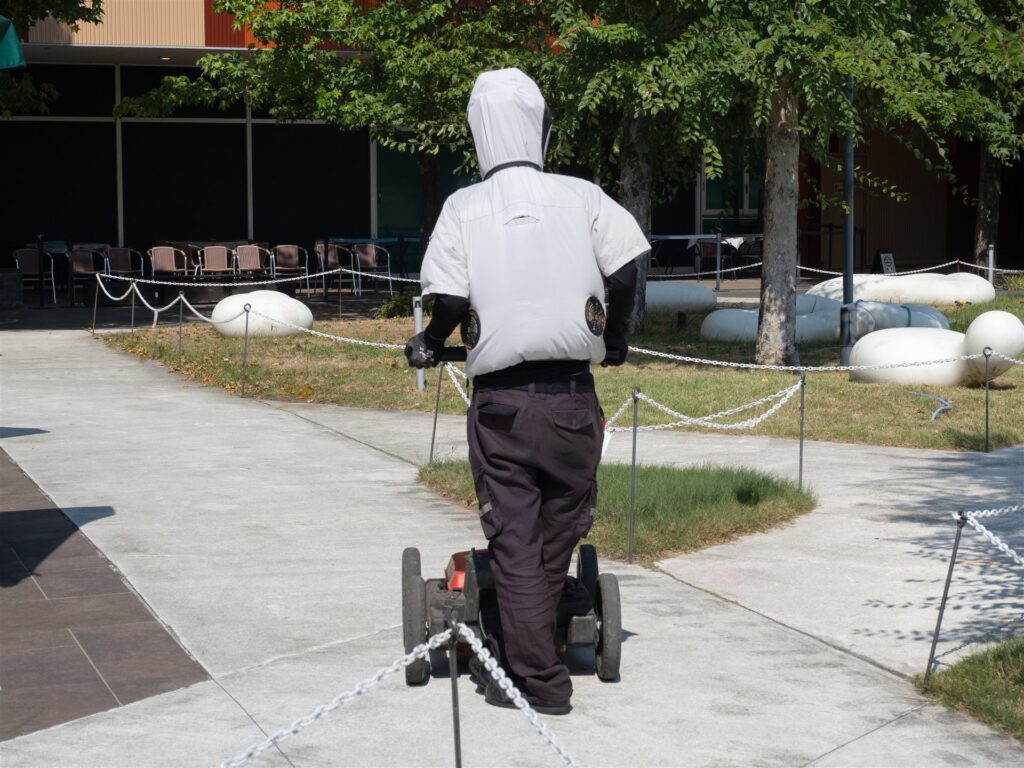 空調服を着て手押しの機械を押す人の後ろ姿