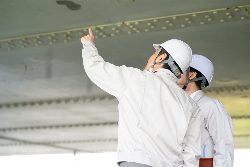 鉄骨の梁を指さして点検するヘルメットの2人