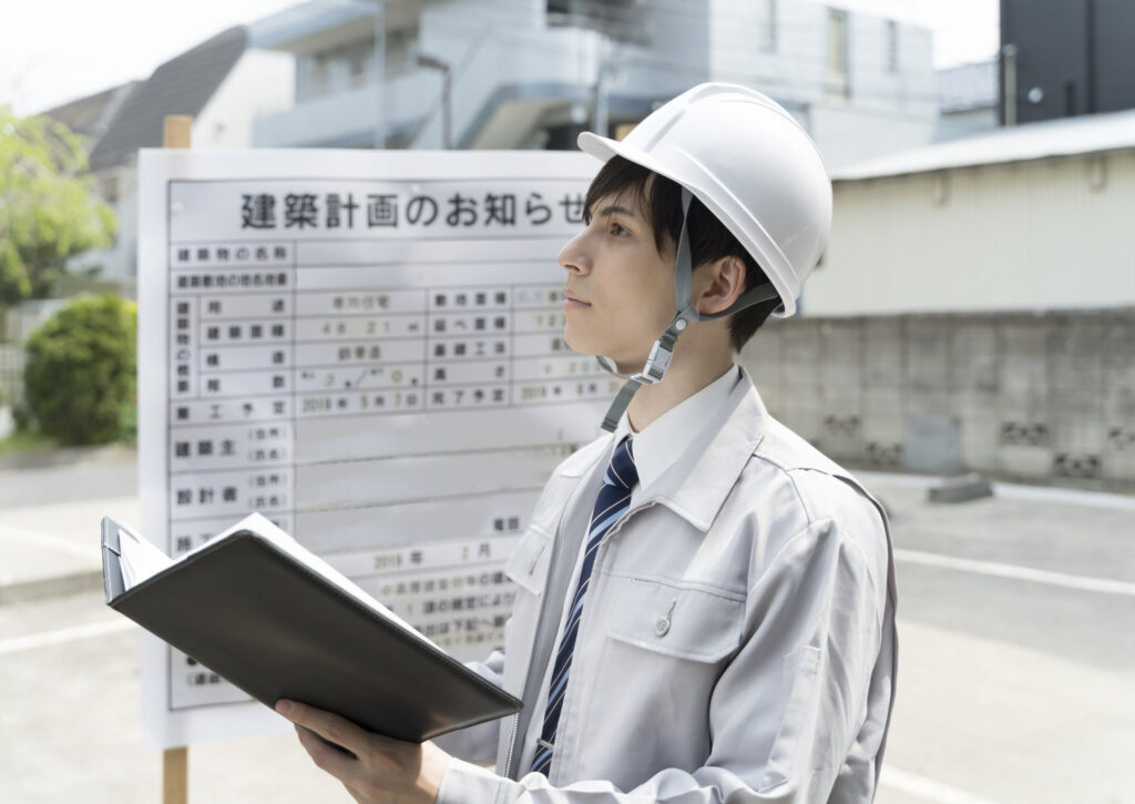 建築計画のお知らせの前でファイルを持つ技術者