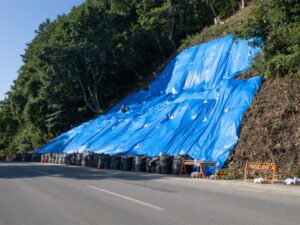 豪雨の後の土砂崩れの法面に青いシートをかけた道路脇