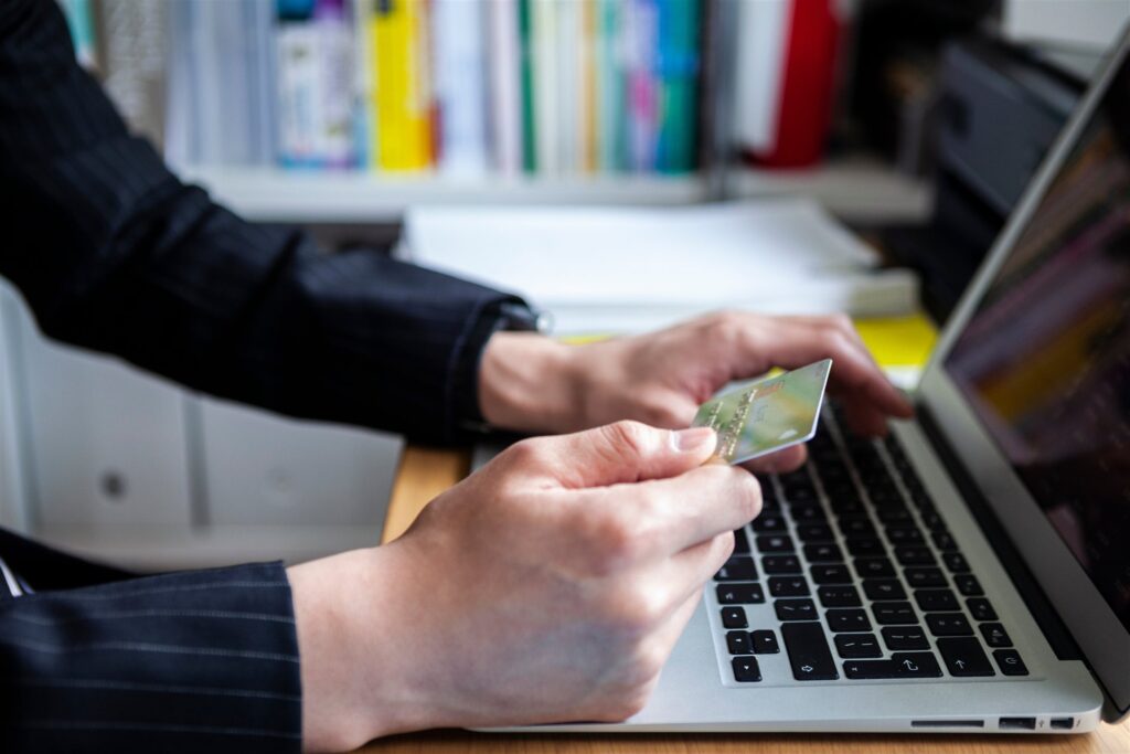 クレジットカードを持ちノートパソコンに向かう手元