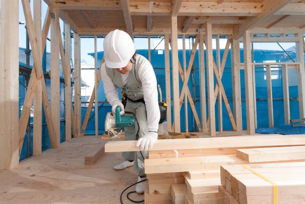 建築中の住宅で材木を電動のこぎりで切る大工