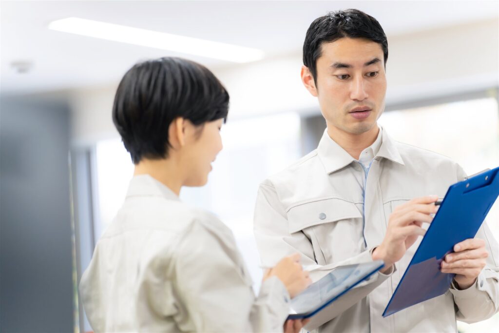 作業服の2人がクリップボードとタブレットで打ち合わせ