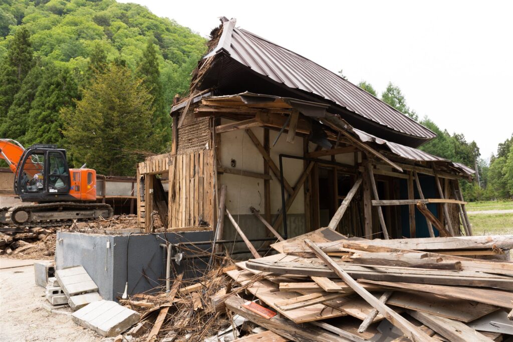 山あいの古い木造の家と解体の重機