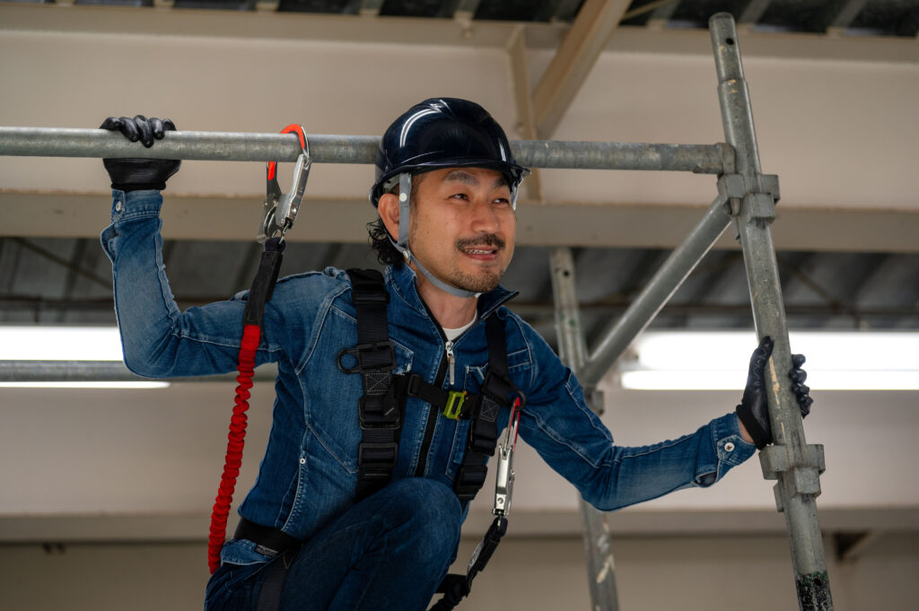 足場の上で安全帯を付けた作業員が手すりを点検する
