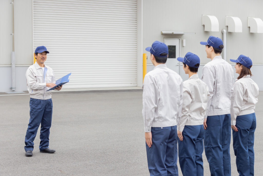 建物の前で作業員が並び責任者が朝礼をする