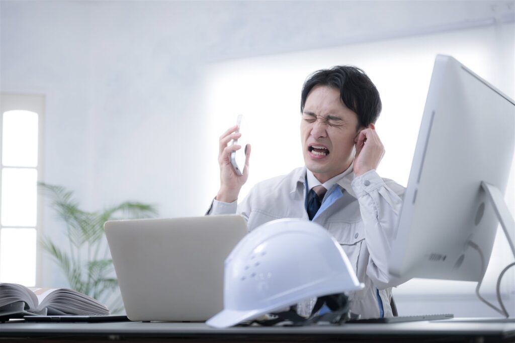 事務所で電話を受けて困った顔の作業着の男性