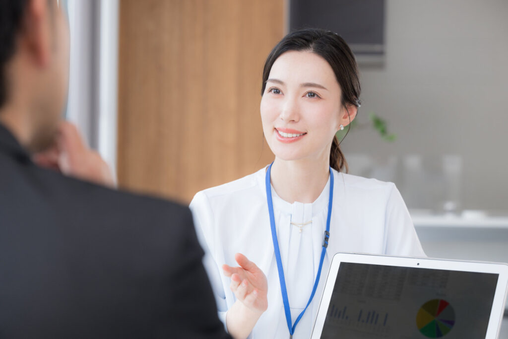 名札の女性がノートパソコンを前に来た人に説明する様子