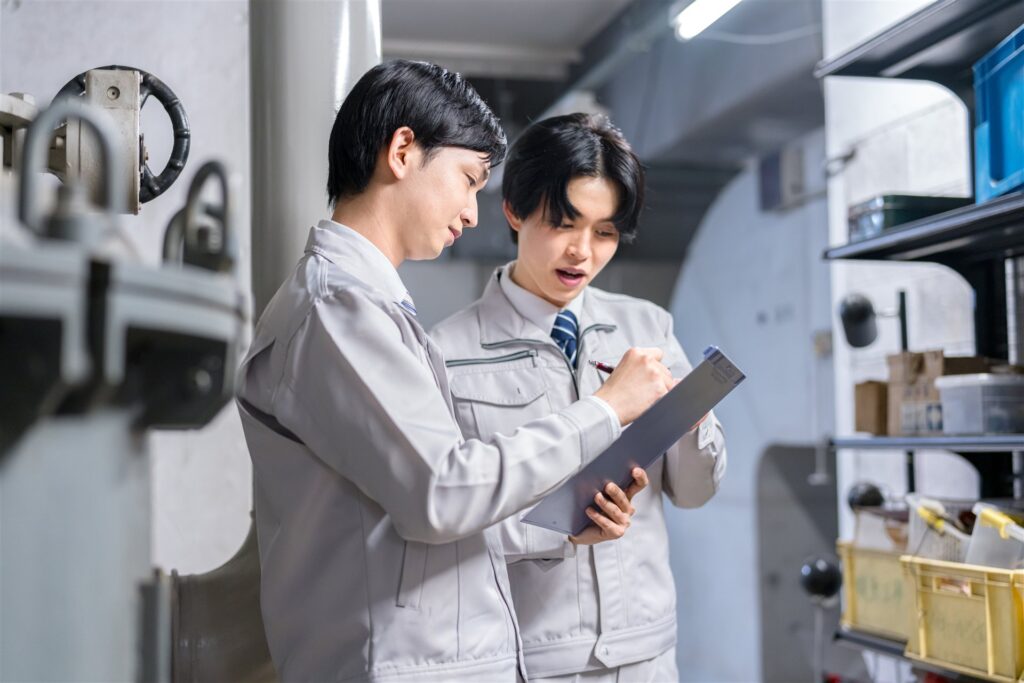 機械室でクリップボードに書く作業着の2人