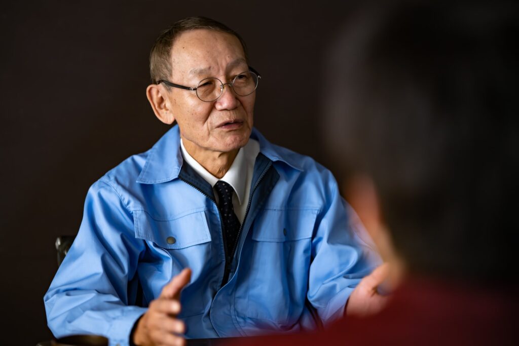 作業着の年配の男性が向かいの人に話す相談の場面