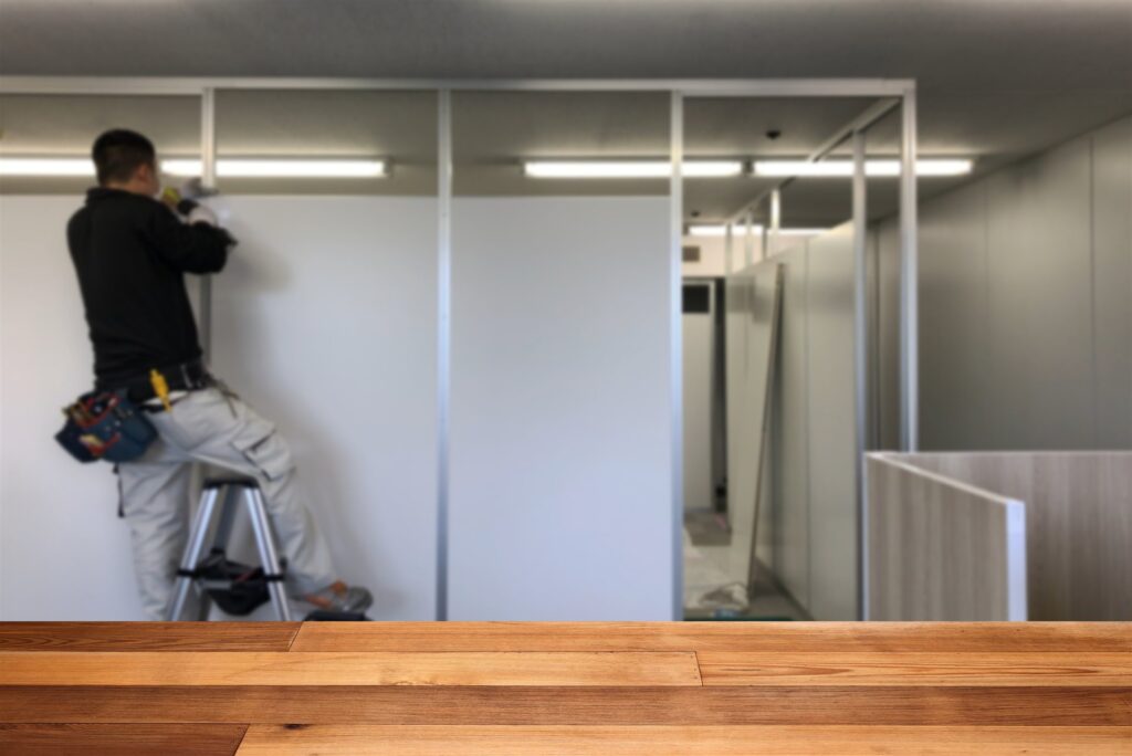 脚立に乗り間仕切りのパネルを付ける職人