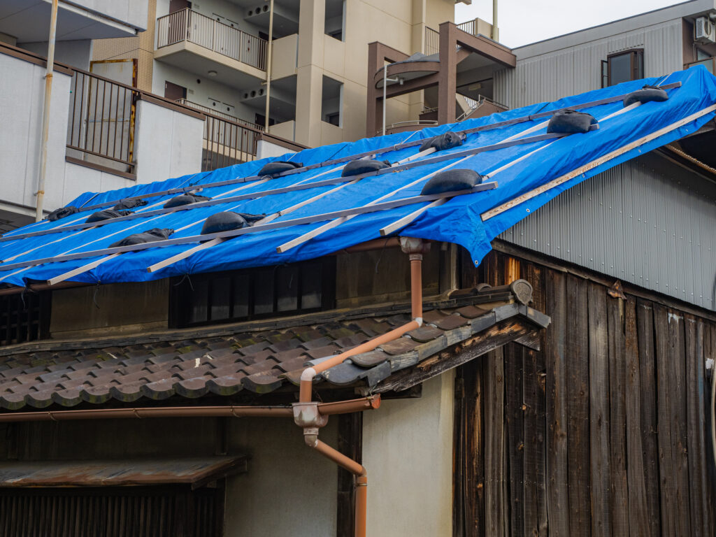 ブルーシートと土のうで覆われた瓦屋根の家