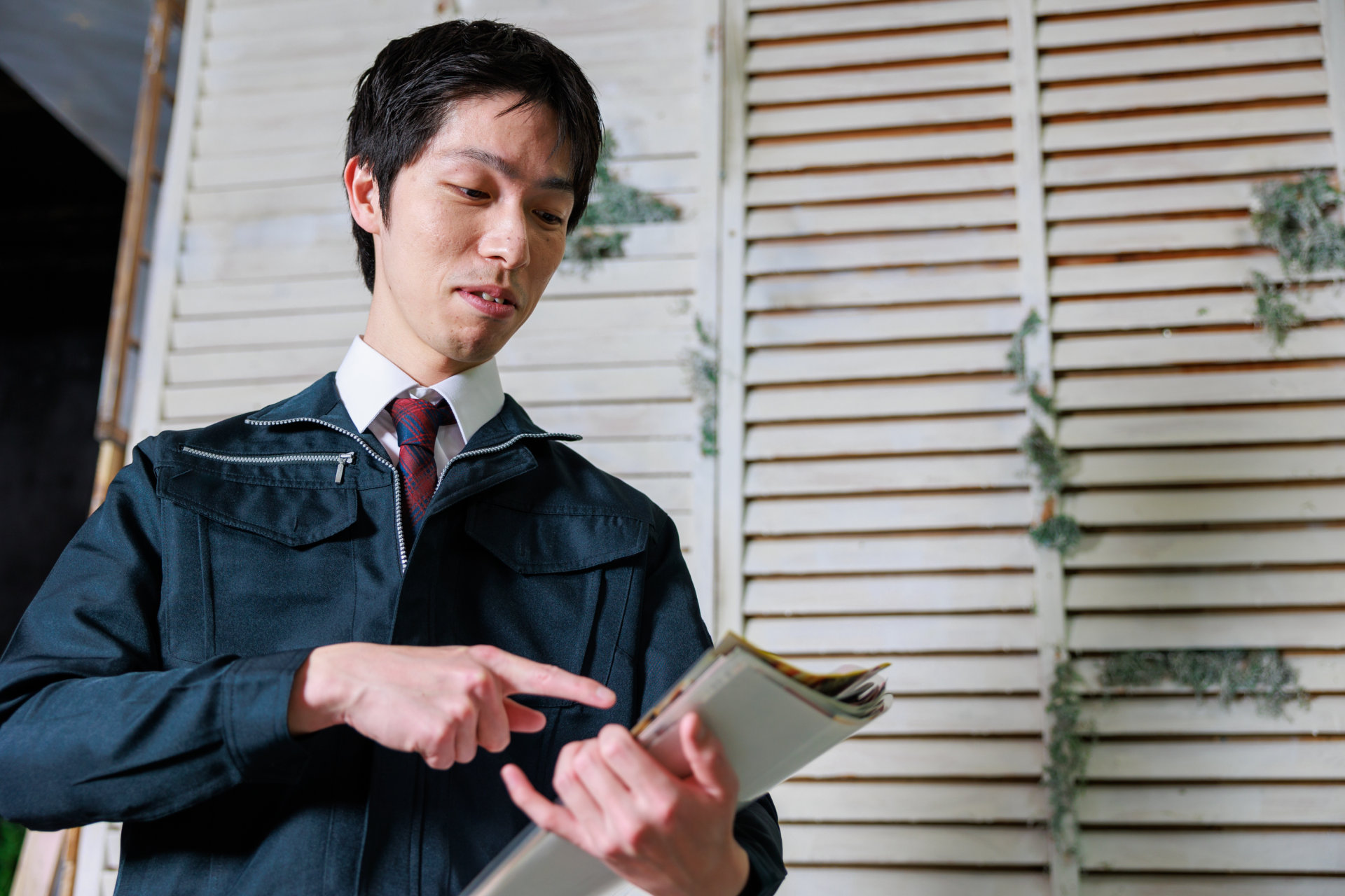 作業服にネクタイの男性が手元の冊子を指さして見直す