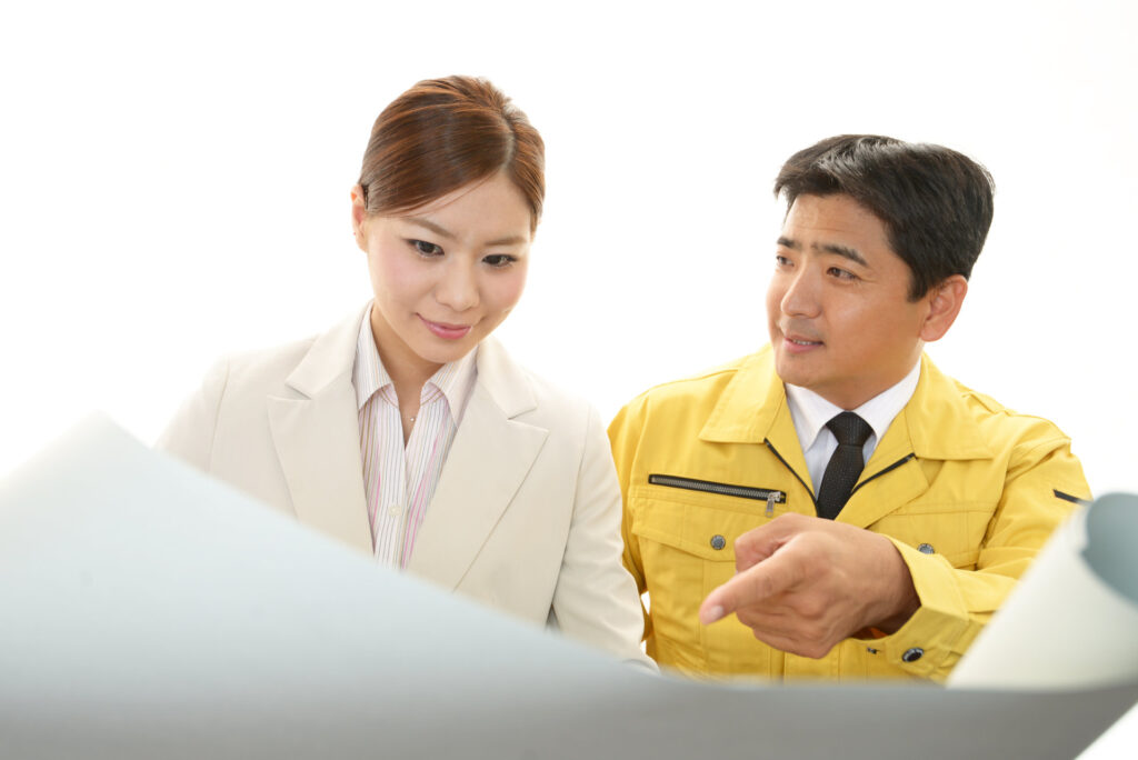 作業服とスーツの2人が書類を確かめる