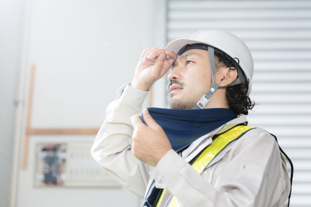 ヘルメット姿の作業員が首元の汗をぬぐう様子