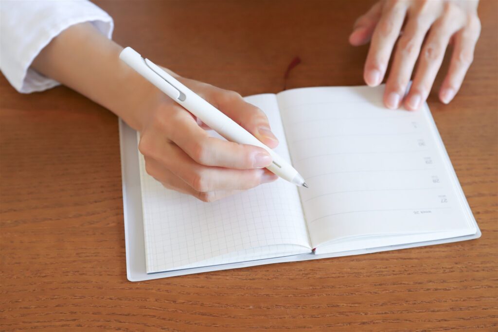 木の机で手帳を開きペンで書き込む手元