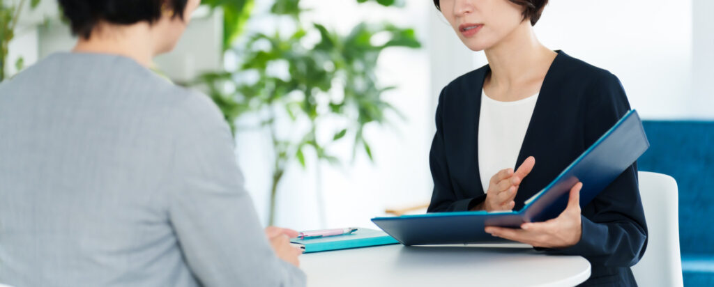 事務所で書類を広げて打ち合わせる二人の女性