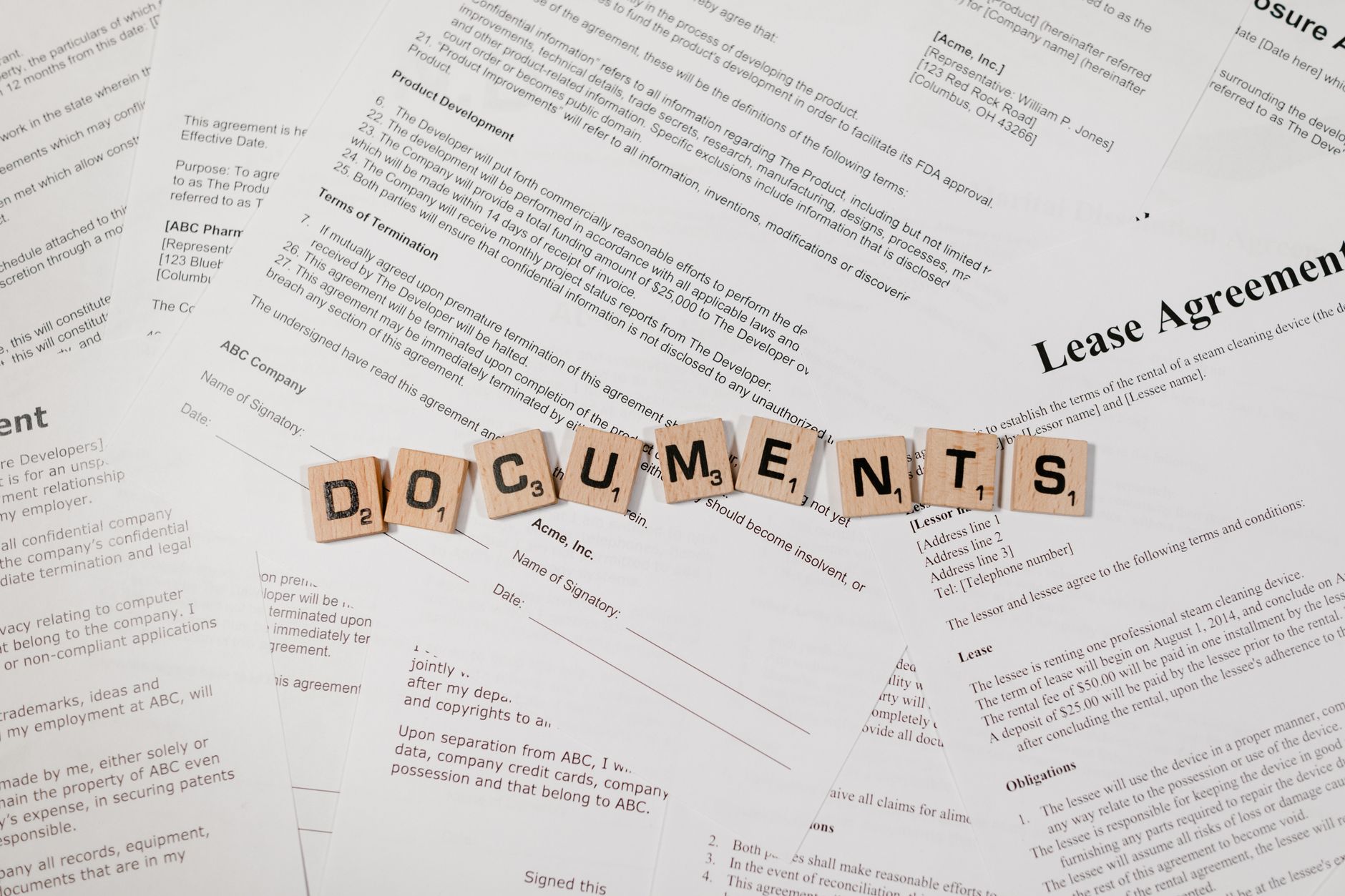 Top view of scrabble tiles spelling DOCUMENTS on various contracts and agreements.