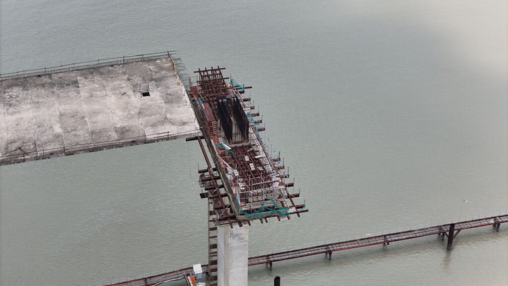 Aerial view of an unfinished bridge structure over water, showcasing construction progress.