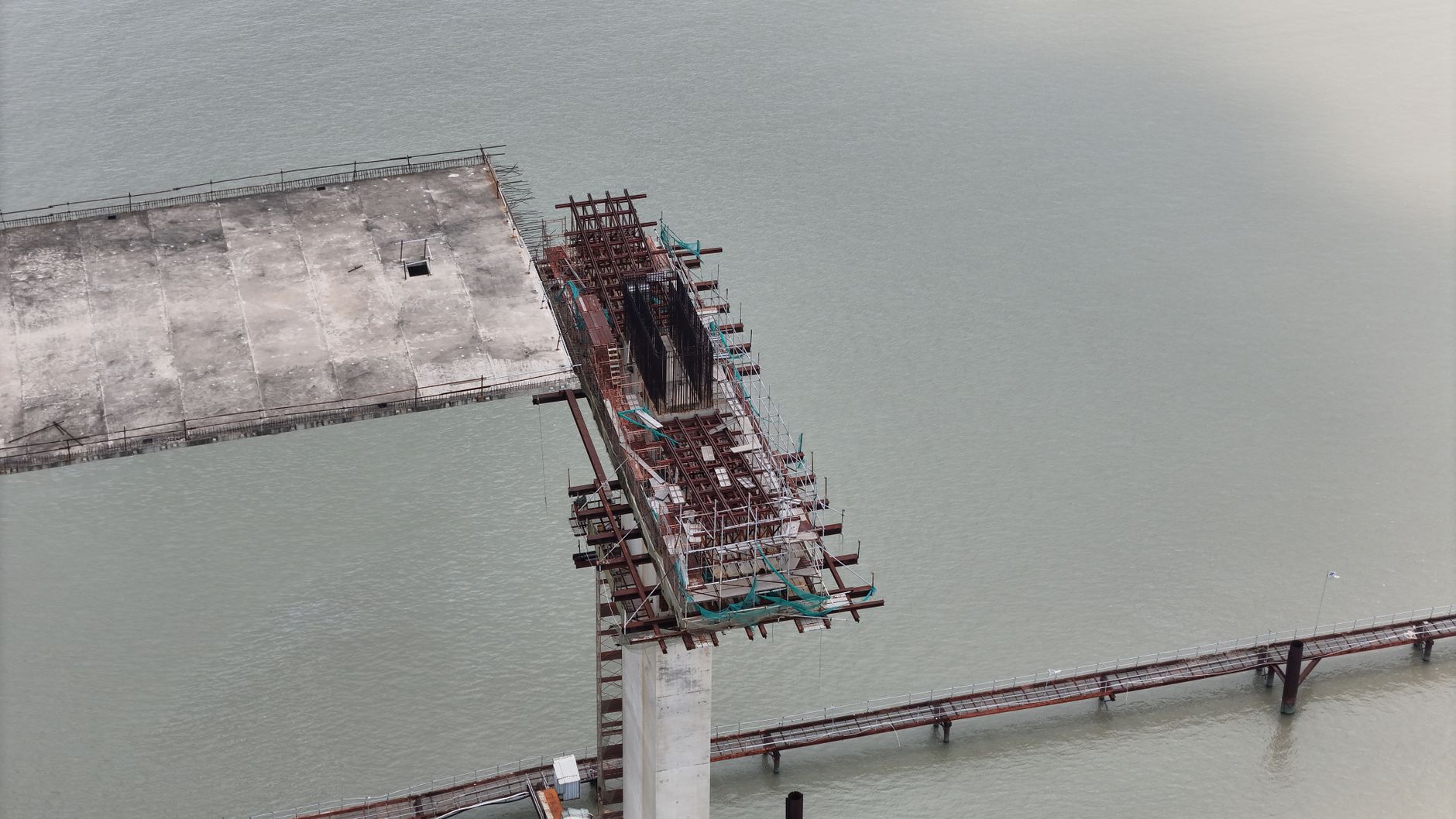 Aerial view of an unfinished bridge structure over water, showcasing construction progress.