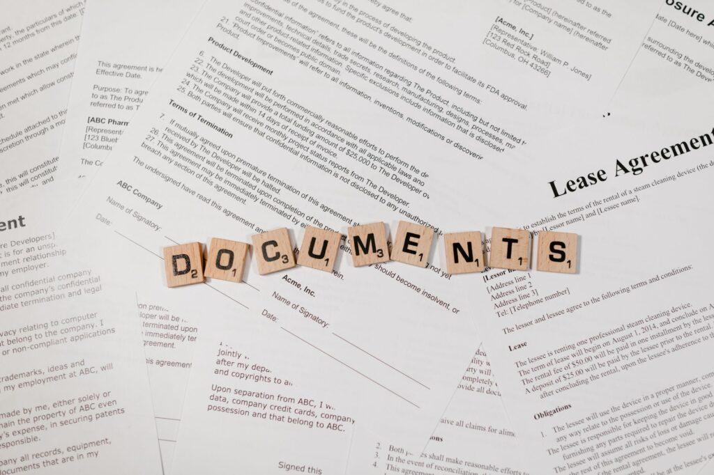 Top view of scrabble tiles spelling DOCUMENTS on various contracts and agreements.