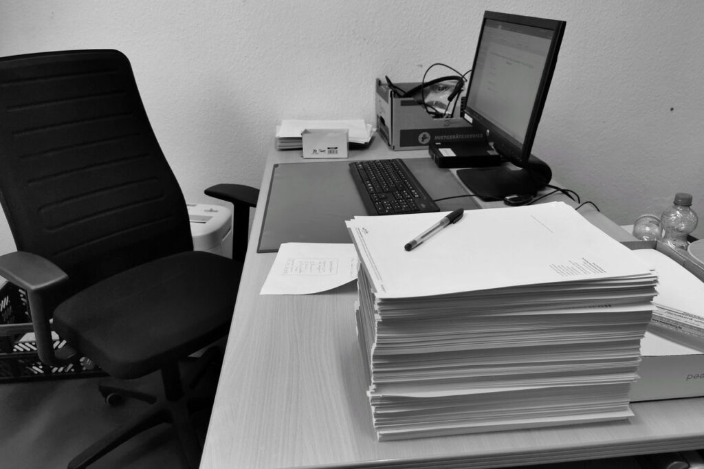 事務所の机に積んだ書類とパソコン