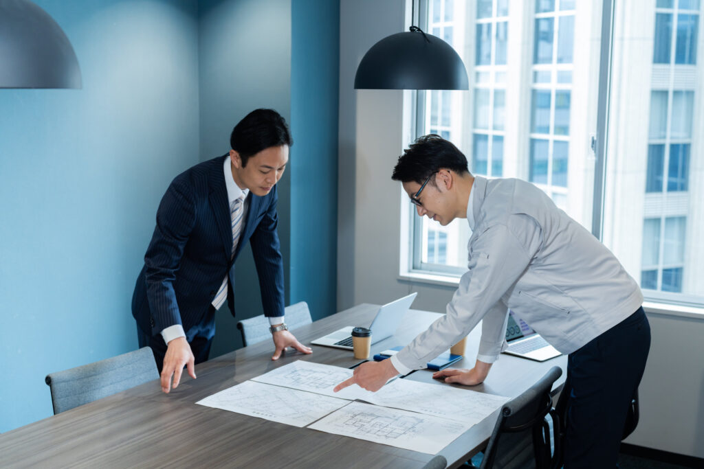 会議室で図面を広げて話し合う2人