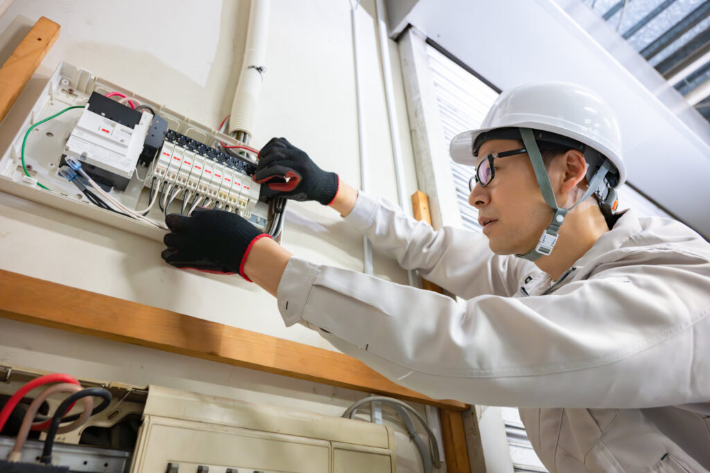 配電盤を点検する作業着とヘルメットの作業員