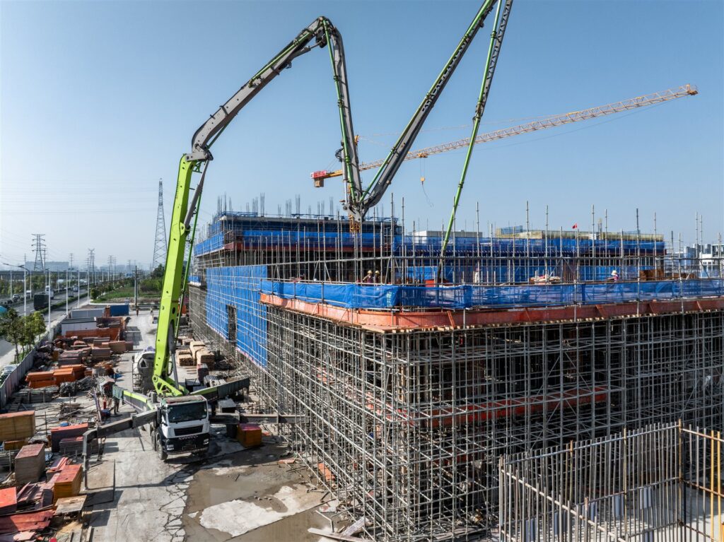 コンクリートポンプ車が並ぶ大きな建物の建設現場