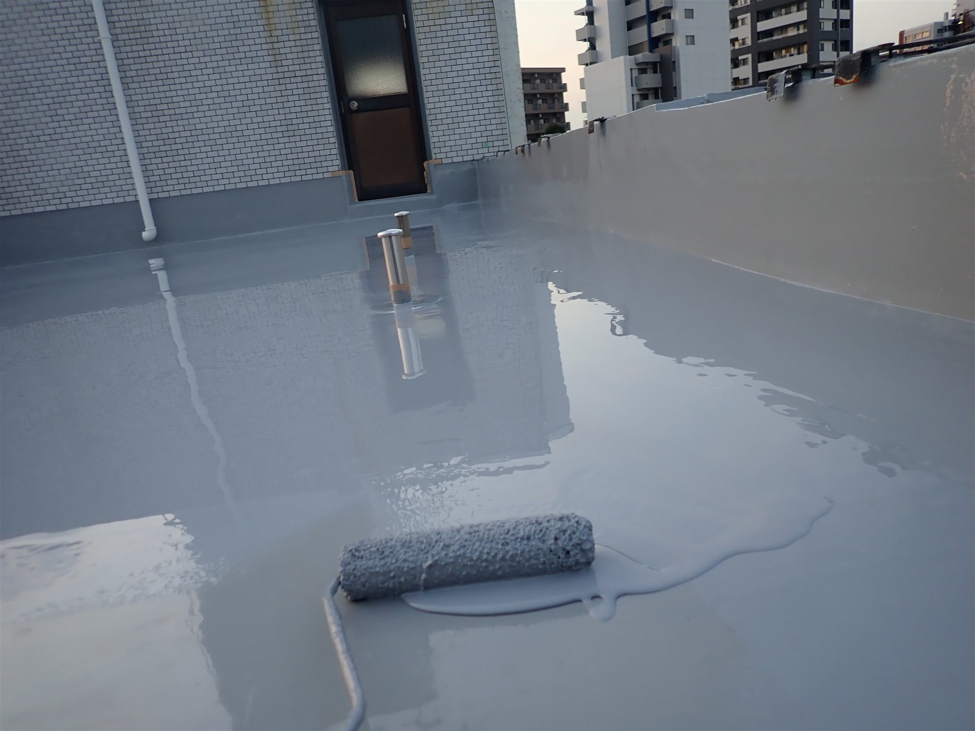屋上の床に塗られたばかりの防水材とローラー