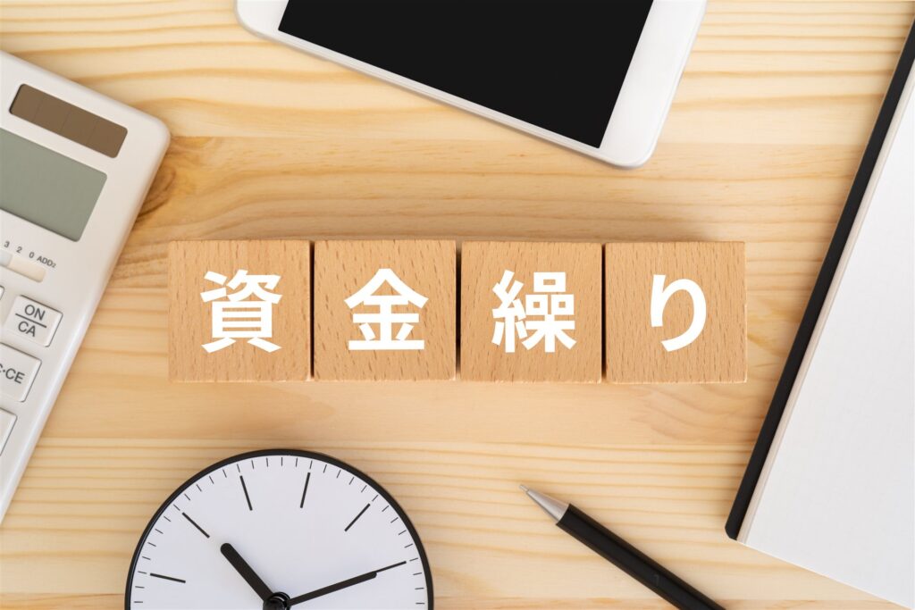 資金繰りと書かれた木の積み木と電卓と時計