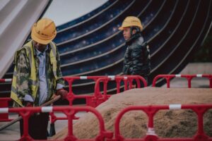 Construction workers with safety gear managing a sand pile outdoors on an urban site.