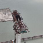 Aerial view of an unfinished bridge structure over water, showcasing construction progress.