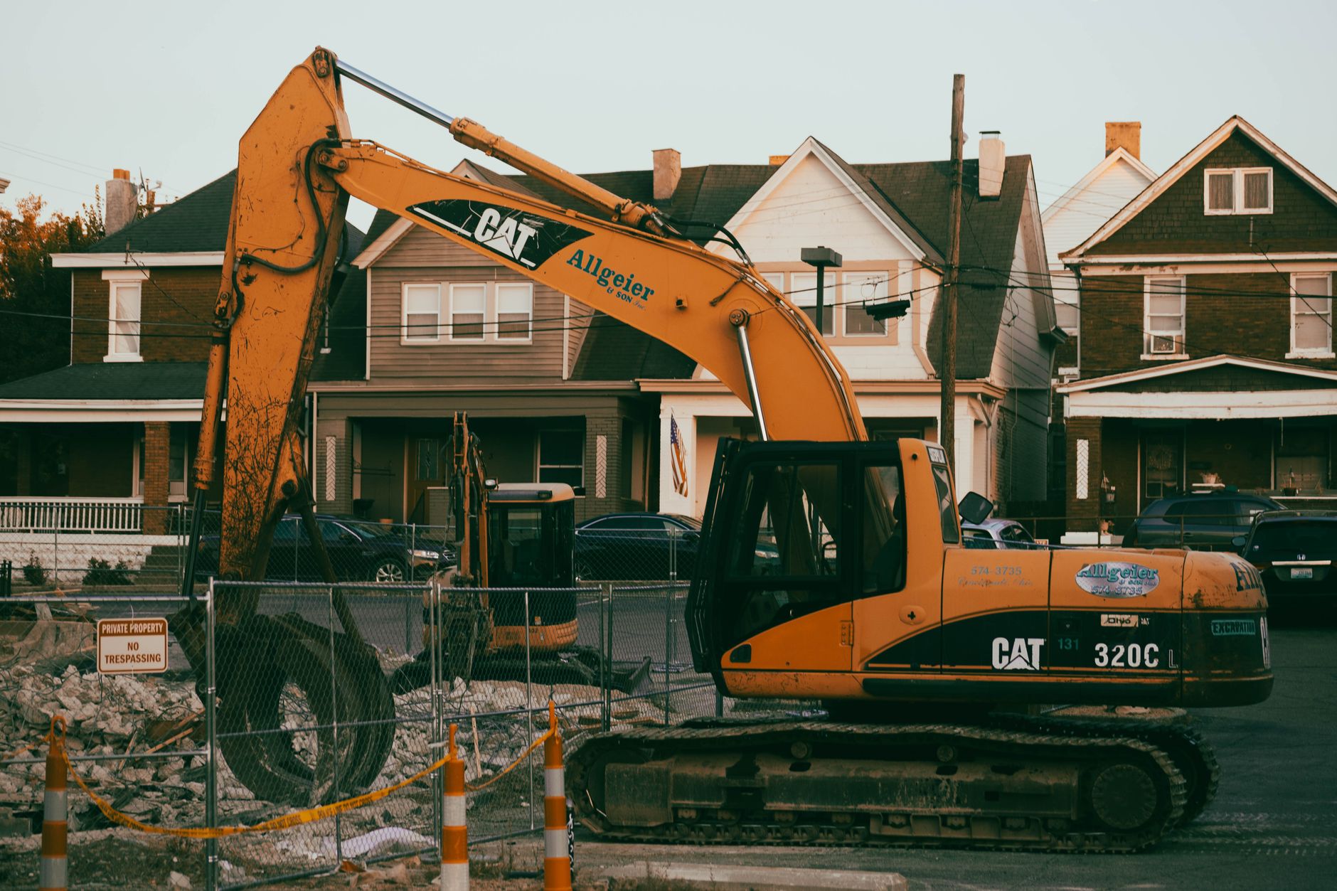 Excavator working in a suburban neighborhood construction site, with residential houses in the background.