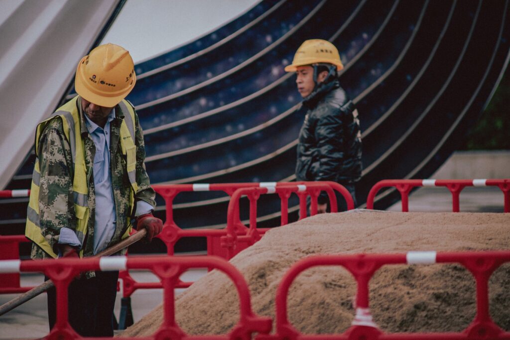 Construction workers with safety gear managing a sand pile outdoors on an urban site.