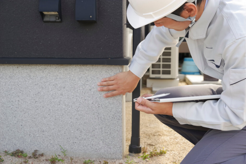 住宅の基礎に手を当てて点検する作業員