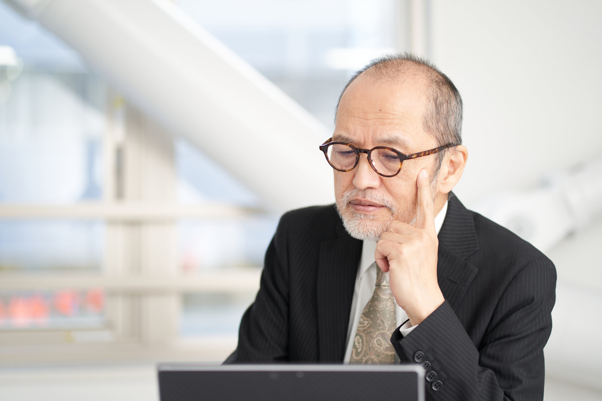 眼鏡の年配の経営者がパソコンの前で考え込む