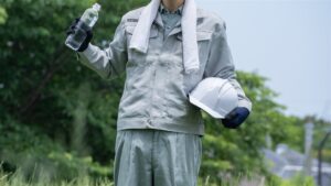 タオルを首に掛け水のボトルとヘルメットを持つ作業着の人