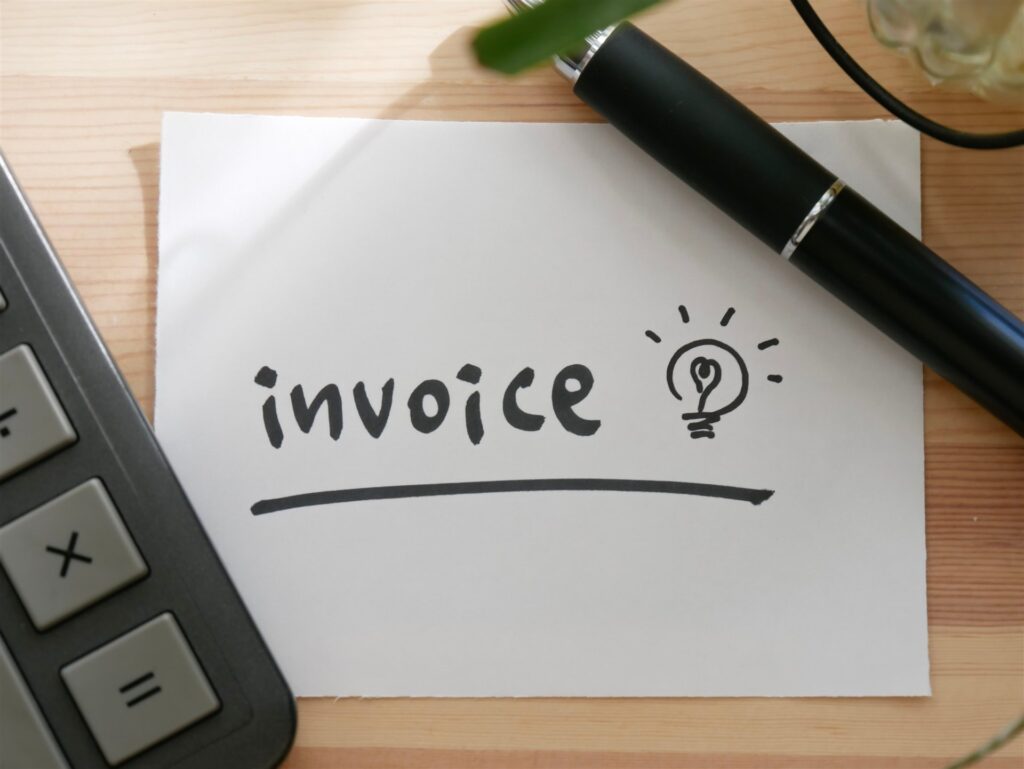 「invoice」と書いた紙と電卓とペン
