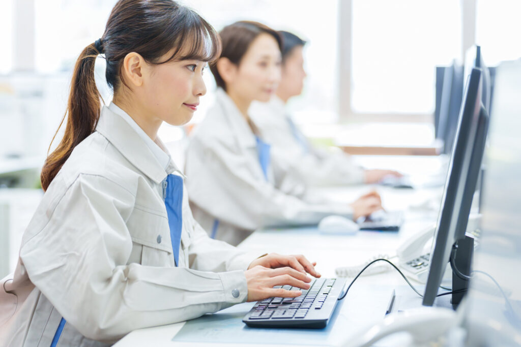 作業服の社員が事務所でパソコンに向かう