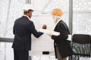 Two architects in hard hats working on a blueprint indoors, highlighting teamwork.