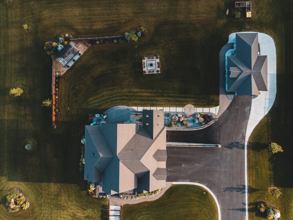 Drone view of suburban neighborhood with houses, driveways, and landscaped gardens.