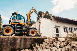 Powerful excavator tearing down an old house during a demolition project outdoors.