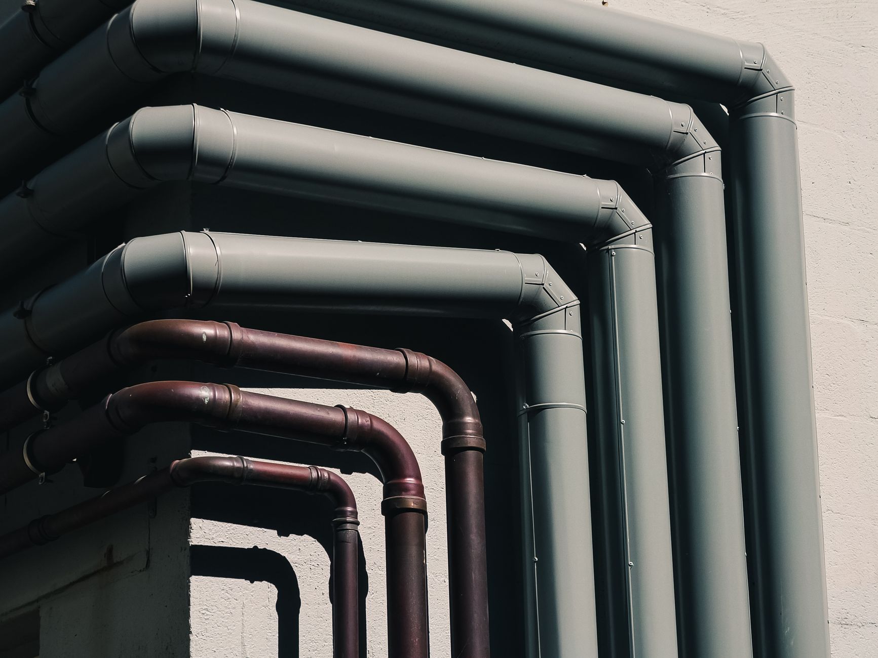 Close-up of industrial pipes forming a pattern on a buildings exterior wall, shot outdoors.
