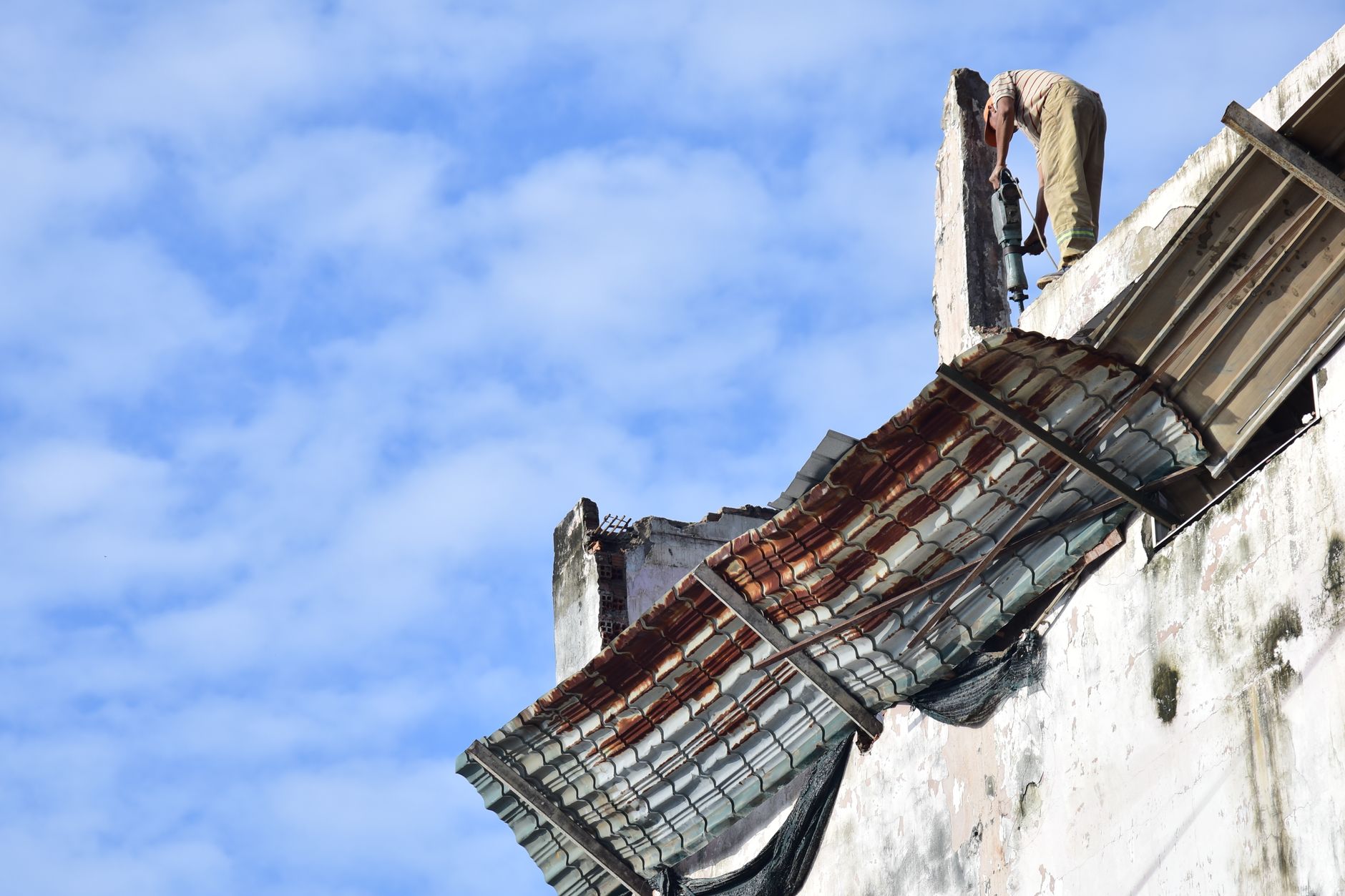 A construction worker repairs a rooftop on a high building under a bright blue sky.