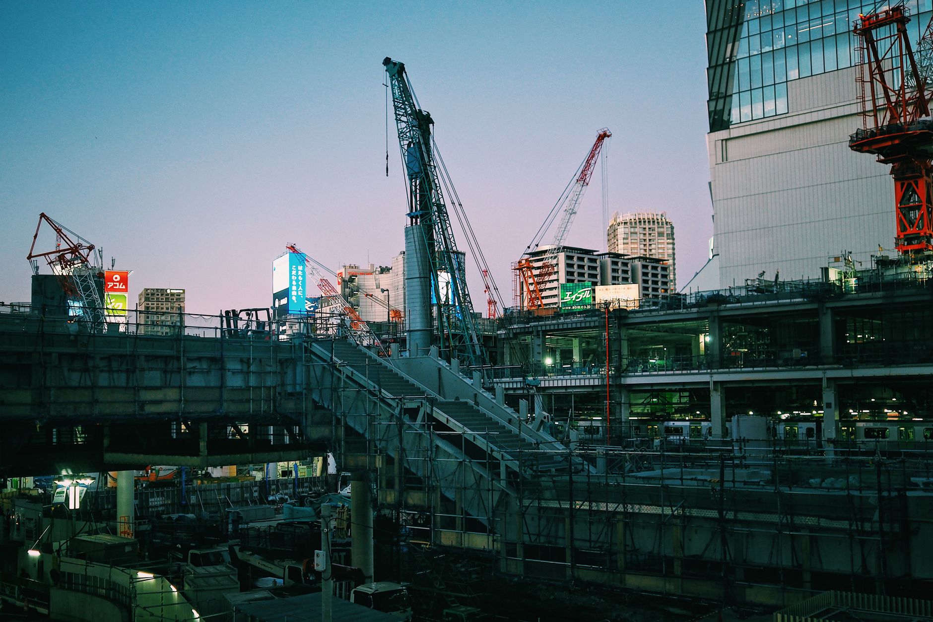 A bustling construction scene in Tokyo, Japan featuring cranes and buildings at dusk.