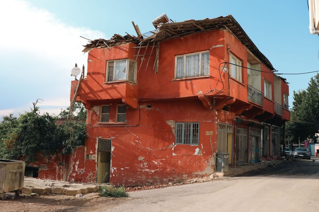 A red building with visible damage, located on a city street corner, under clear skies.