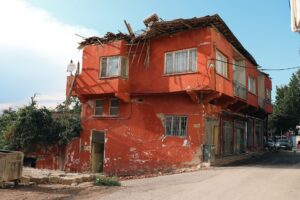 A red building with visible damage, located on a city street corner, under clear skies.