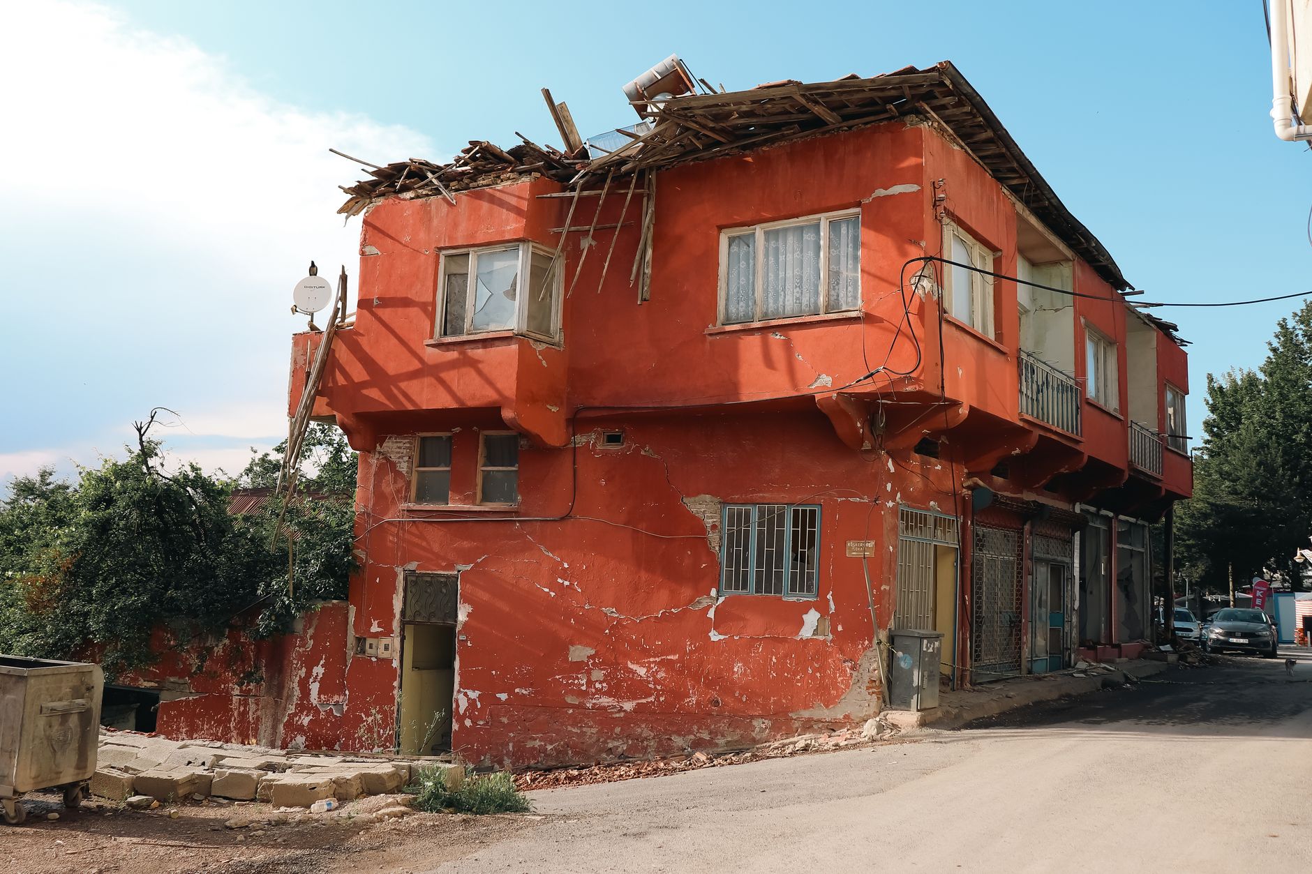 A red building with visible damage, located on a city street corner, under clear skies.